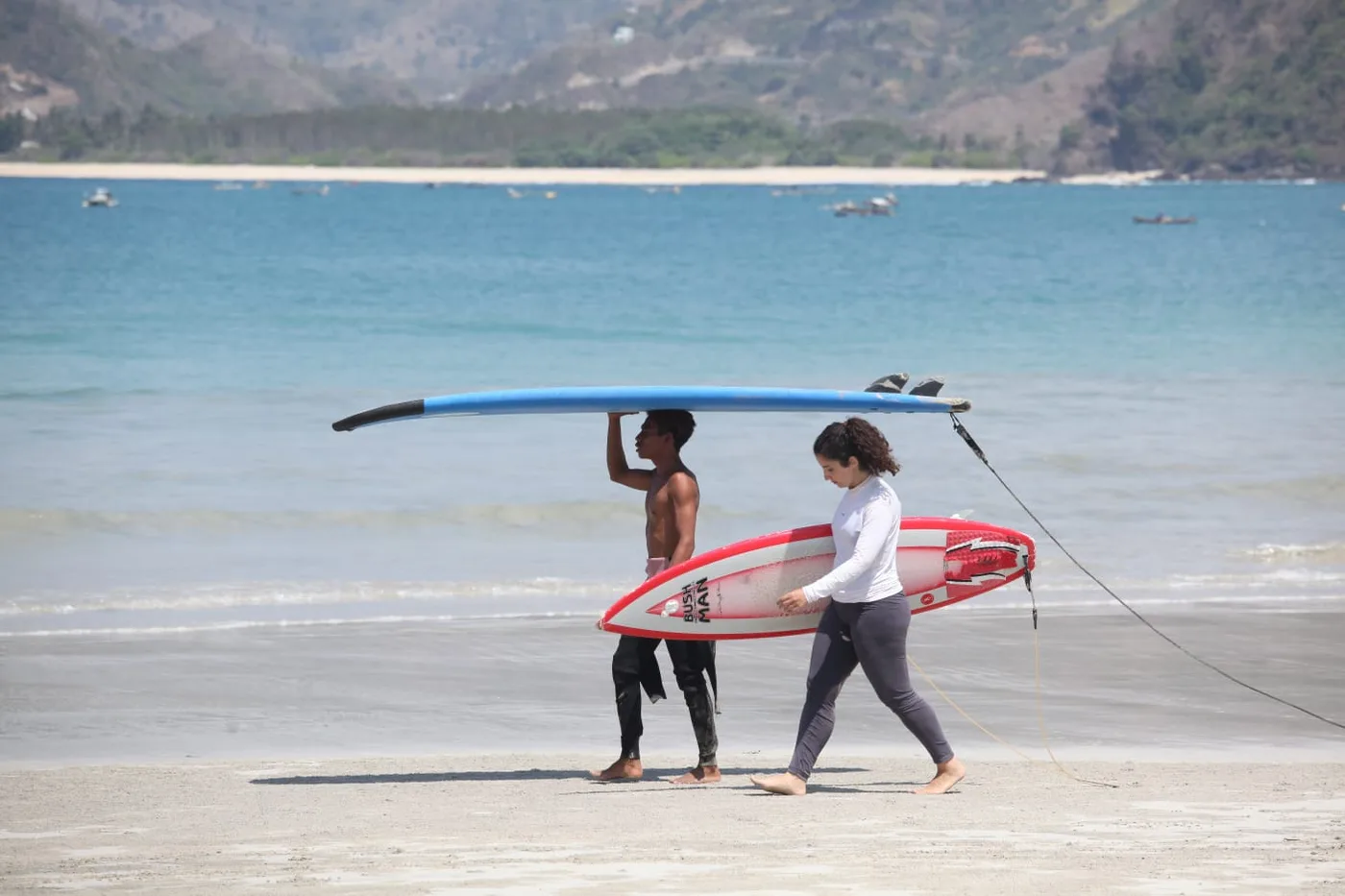 An instructor and a guest carrying surfboards along a beach in Lombok