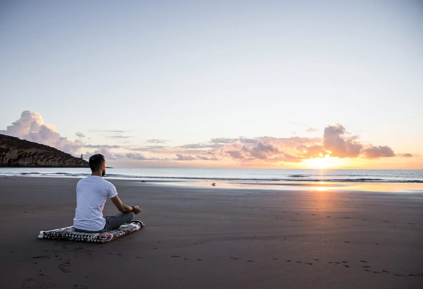 Antonin sitting on a beach, facing the sea at sunset